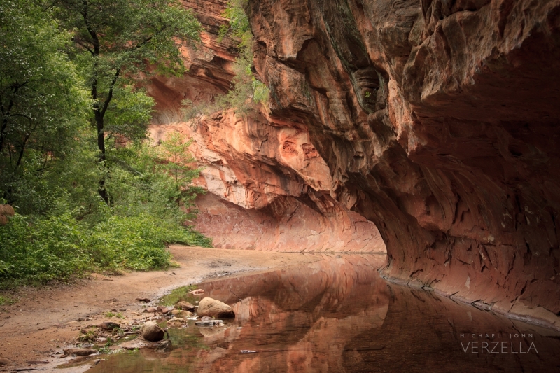 Carved, red rock is reflected in the creek.